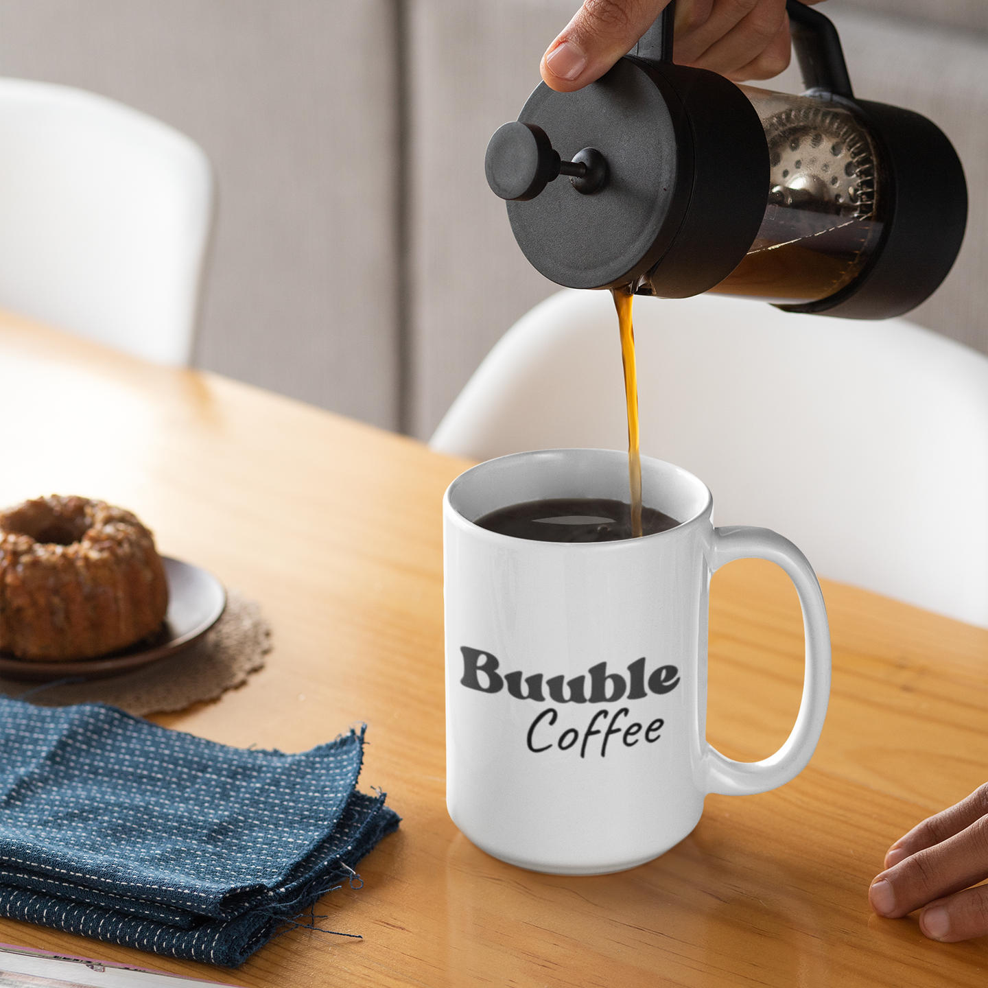 Person pouring coffee from a French press into a white mug with 'Buuble Coffee' text on a wooden table.