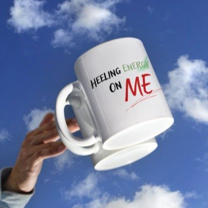 Large white mug with text held against a blue sky with clouds.