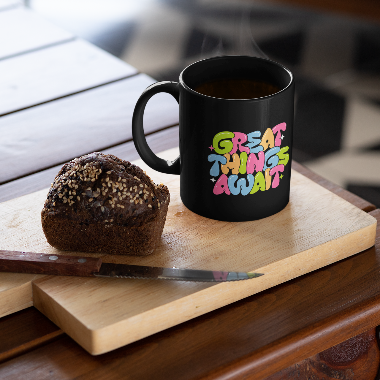 Black mug with colorful text on a wooden cutting board with a muffin and knife.