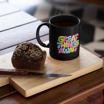 Black mug with colorful text on a wooden cutting board with a muffin and knife.
