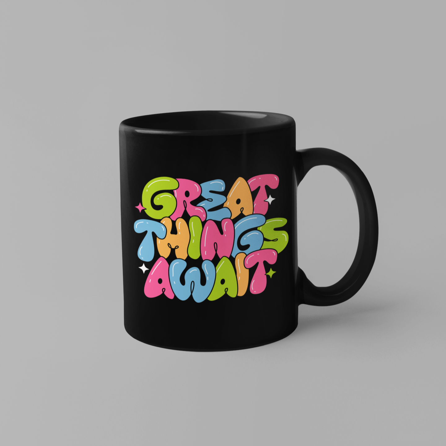 A black ceramic mug with vibrant, colorful lettering that reads 'GREAT THINGS AWAIT' in dripping bubble font.