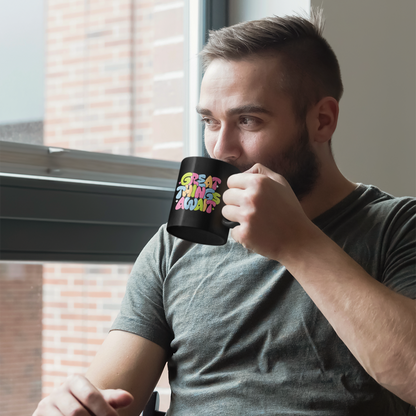 Man holding a black mug with text, sitting by a window.