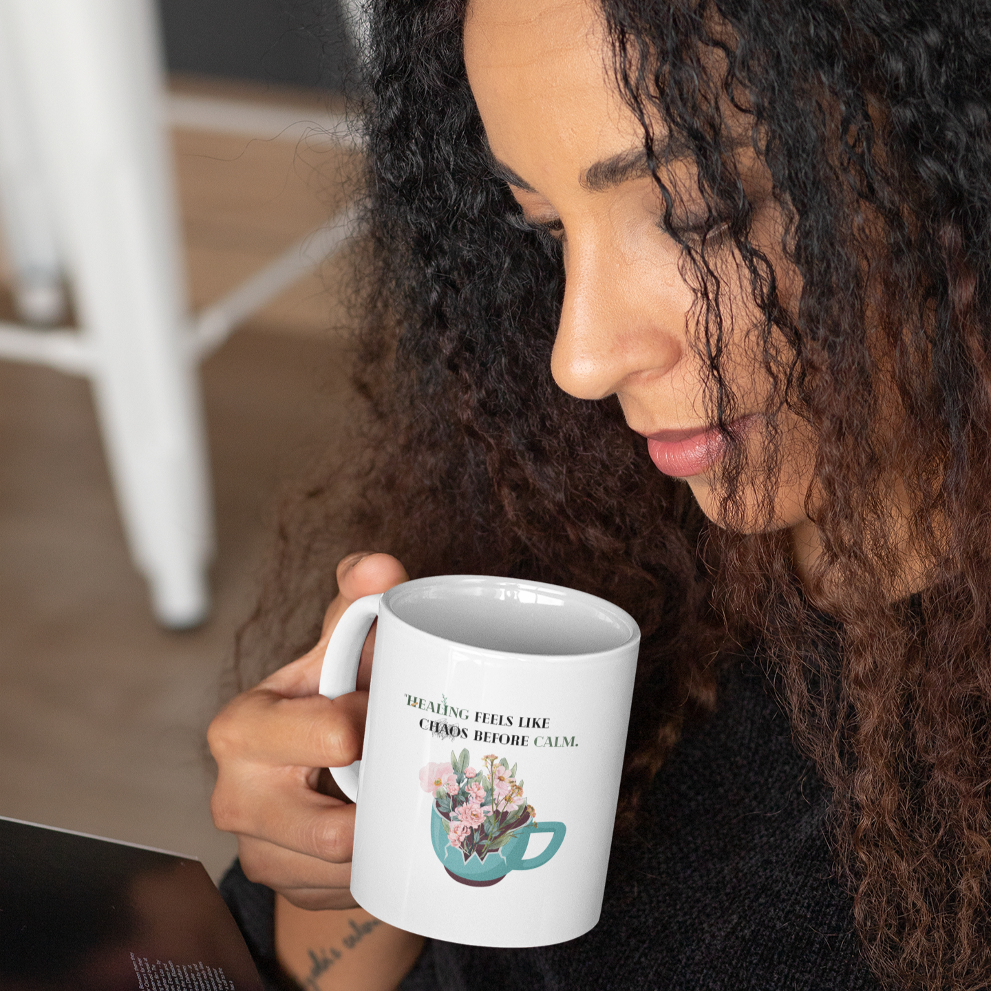 Woman holding a mug with a floral design and text, using a tablet.