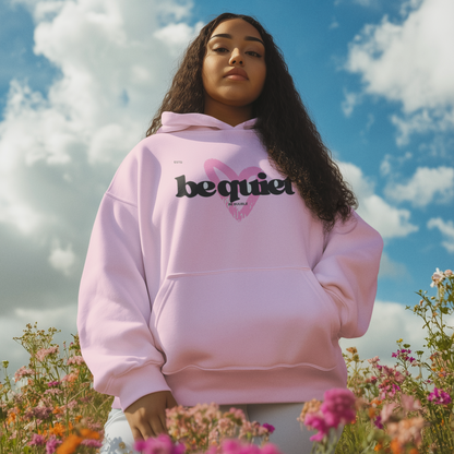 Person wearing a pink hoodie with 'be quiet' text in a field of flowers under a blue sky.