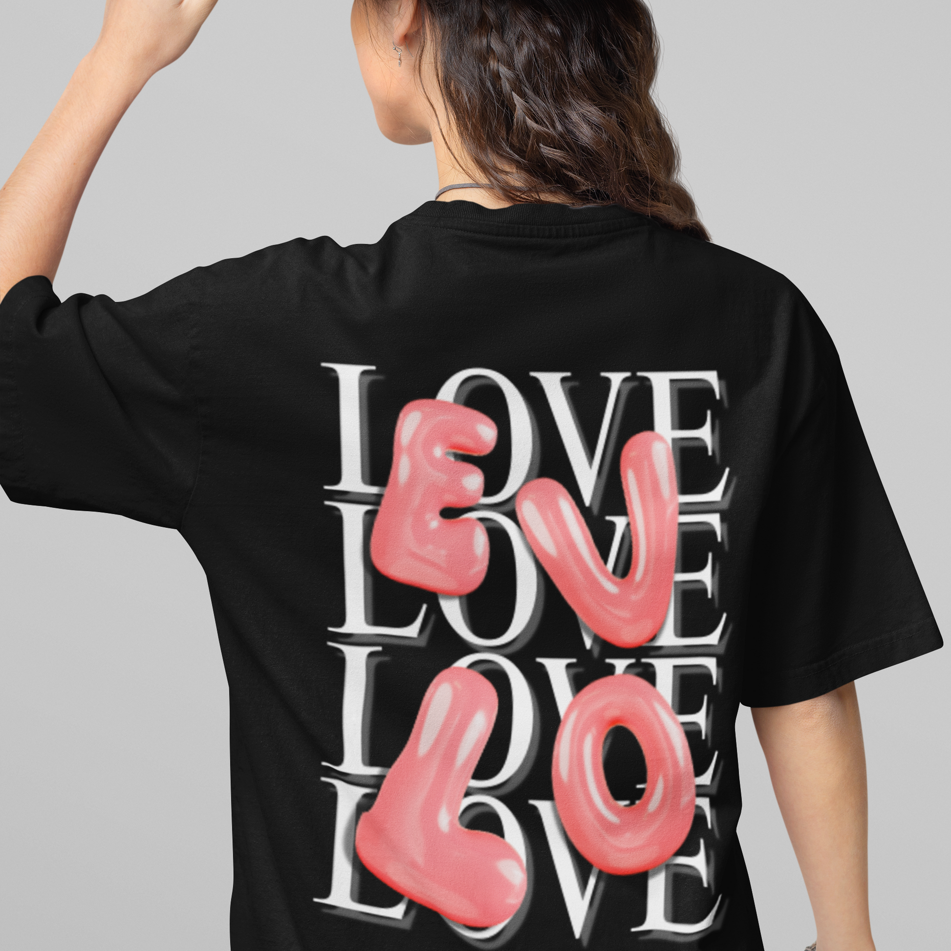Person wearing a black t-shirt with 'LOVE' printed on the back, holding a brown hat.