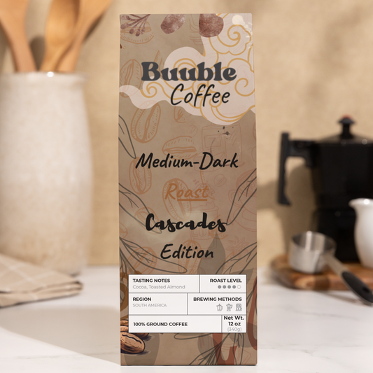 A bag of Buuble Cascades Coffee - Blend Medium-Dark Roast Edition, positioned on a kitchen counter with wooden utensils and kitchen appliances in the background.
