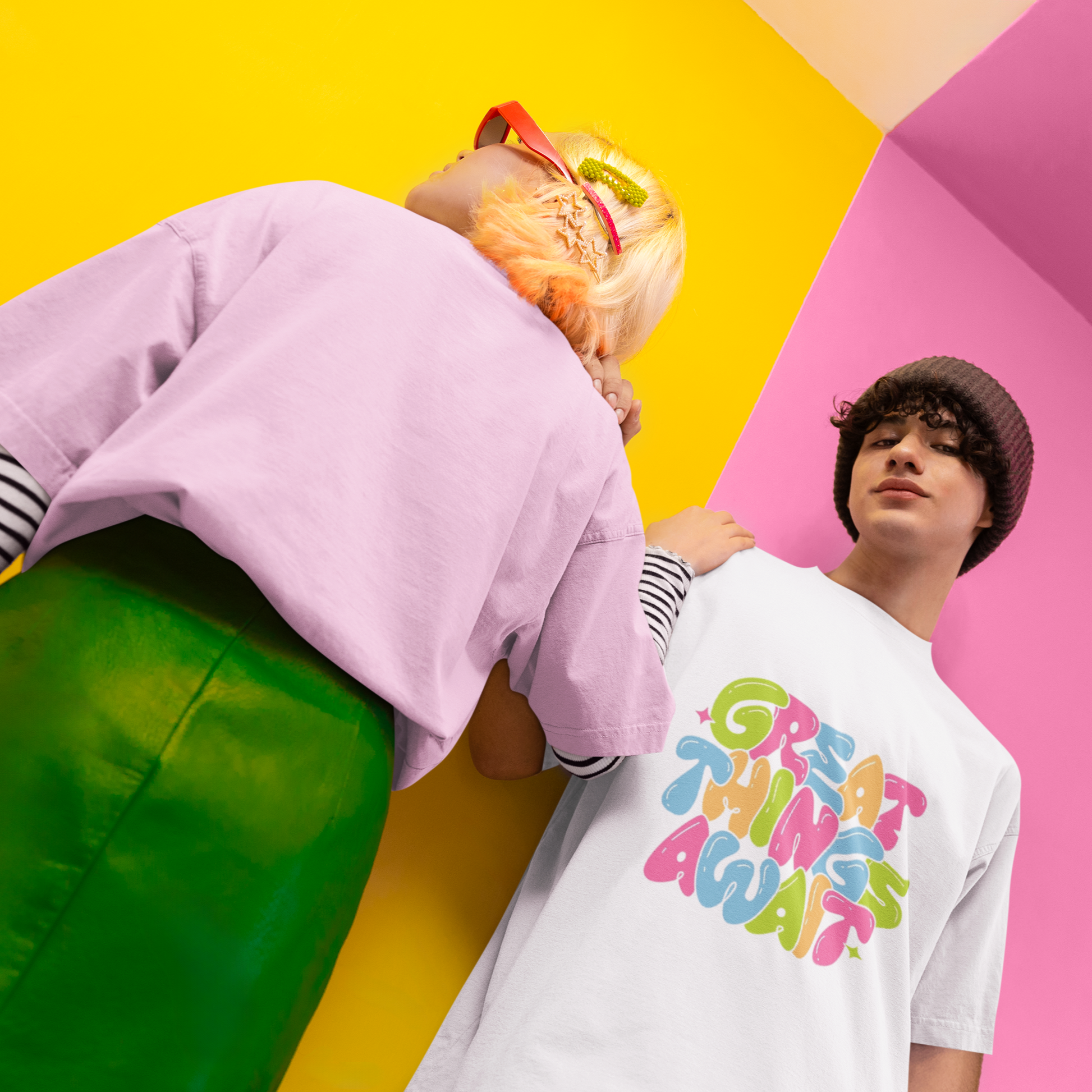 Two people standing on a colorful background with one wearing a white t-shirt with colorful text.