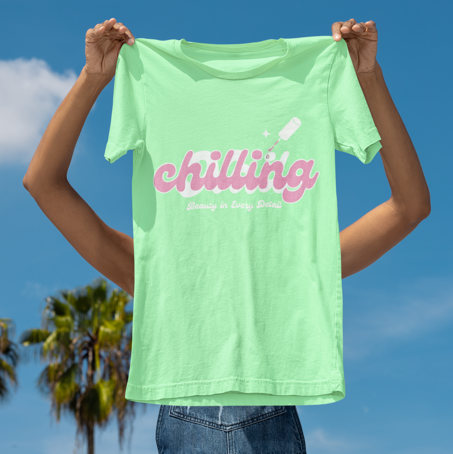 Person holding a green t-shirt with 'chilling' text against a blue sky background
