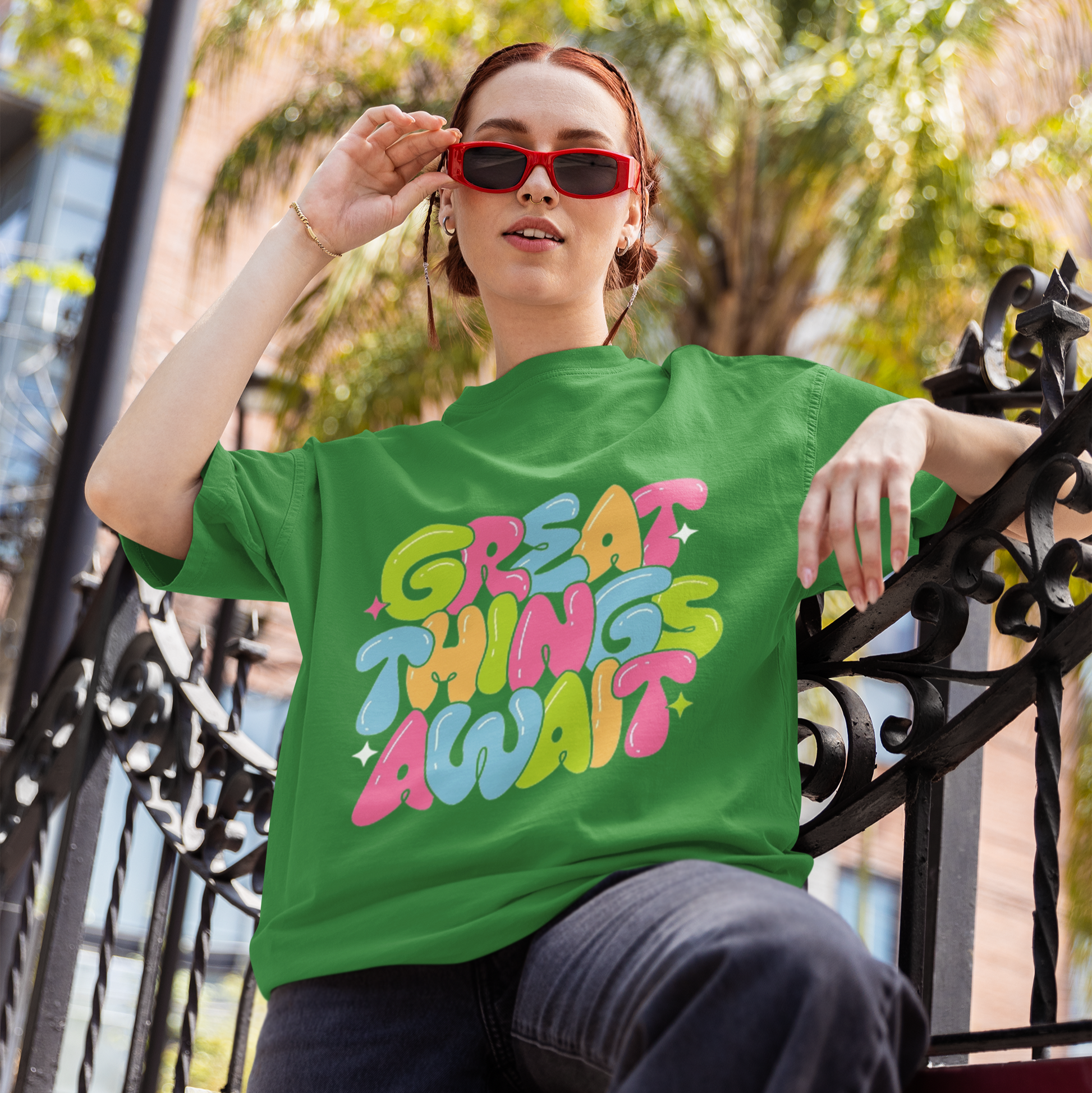 Person wearing a green t-shirt with colorful text, sitting outdoors.