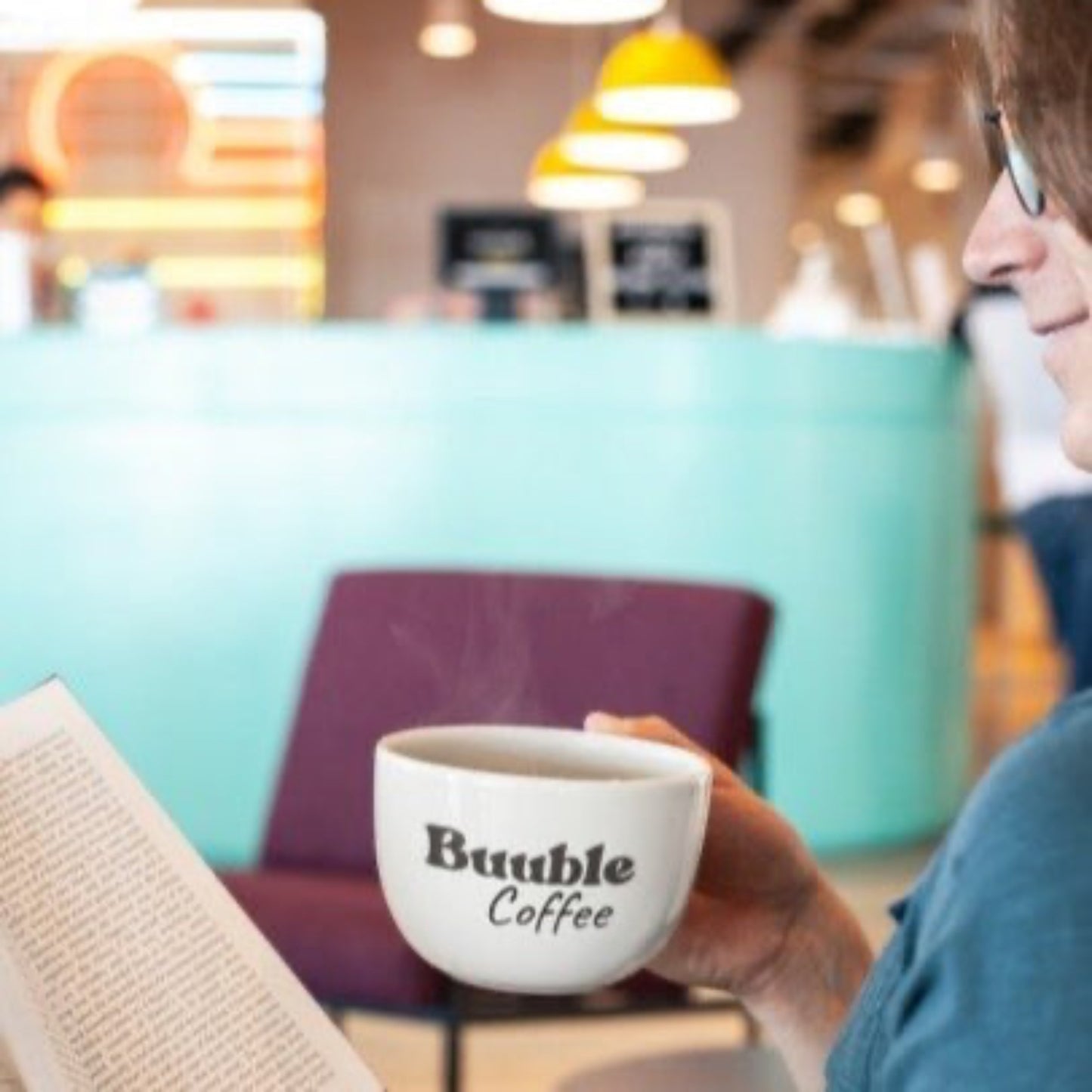 Person holding a 'Buuble Coffee' mug in a blurred cafe setting