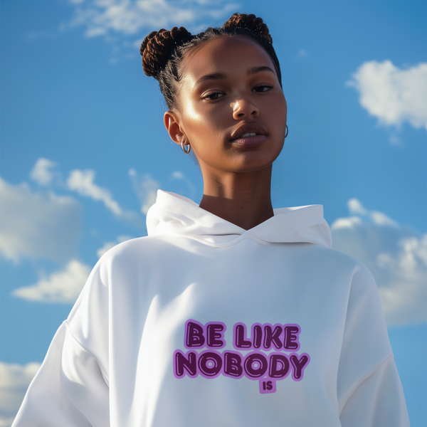 Person wearing a white hoodie with 'BE LIKE NOBODY' text against a blue sky.