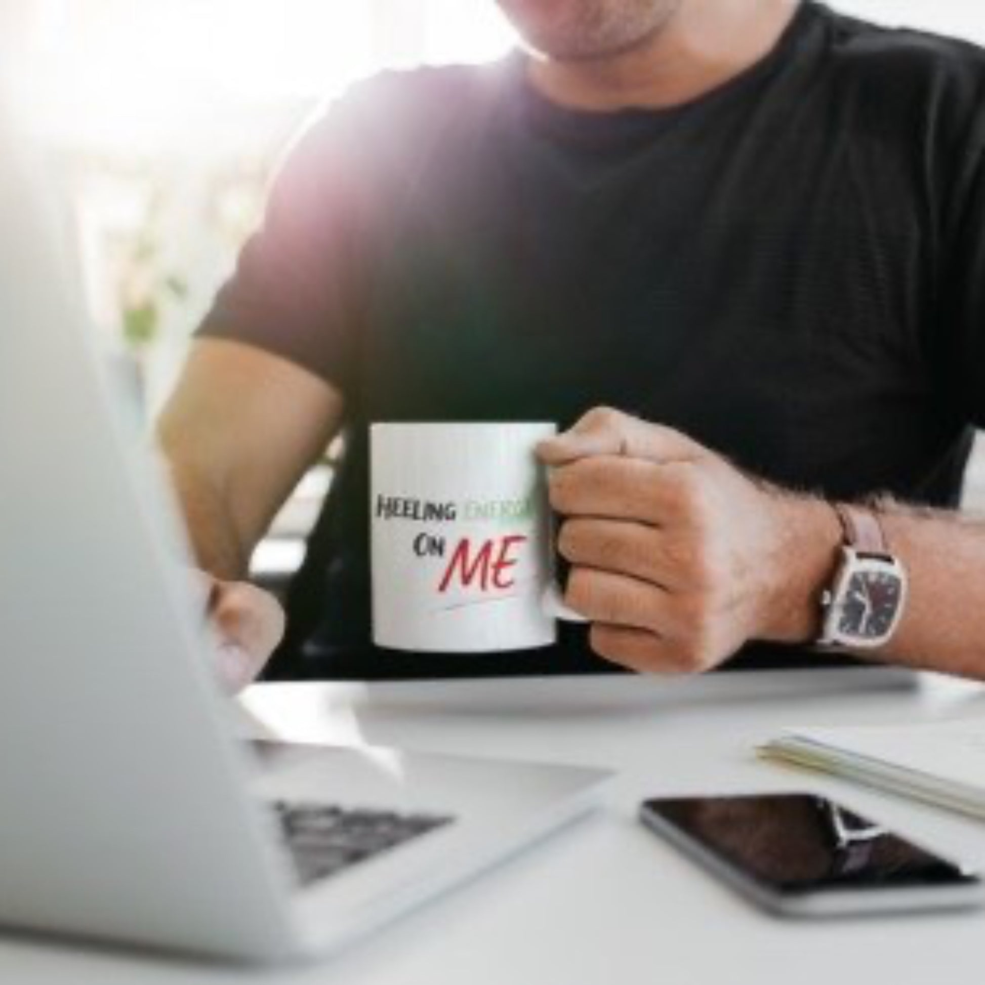 Person holding a mug with text, sitting at a laptop.