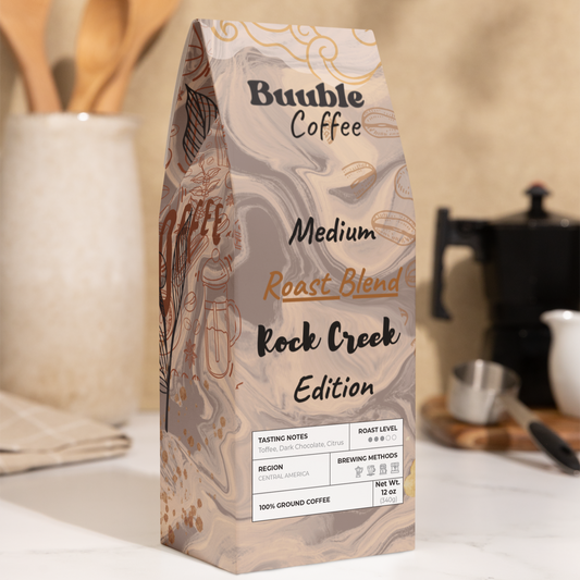A bag of Buuble Coffee Rock Creek Edition with a medium roast blend, placed on a kitchen counter with wooden utensils and a coffee maker in the background.
