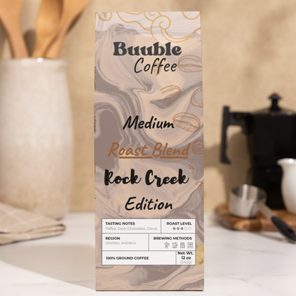 A bag of Buuble Coffee Rock Creek Edition on a kitchen counter with wooden utensils and a coffee maker in the background.
