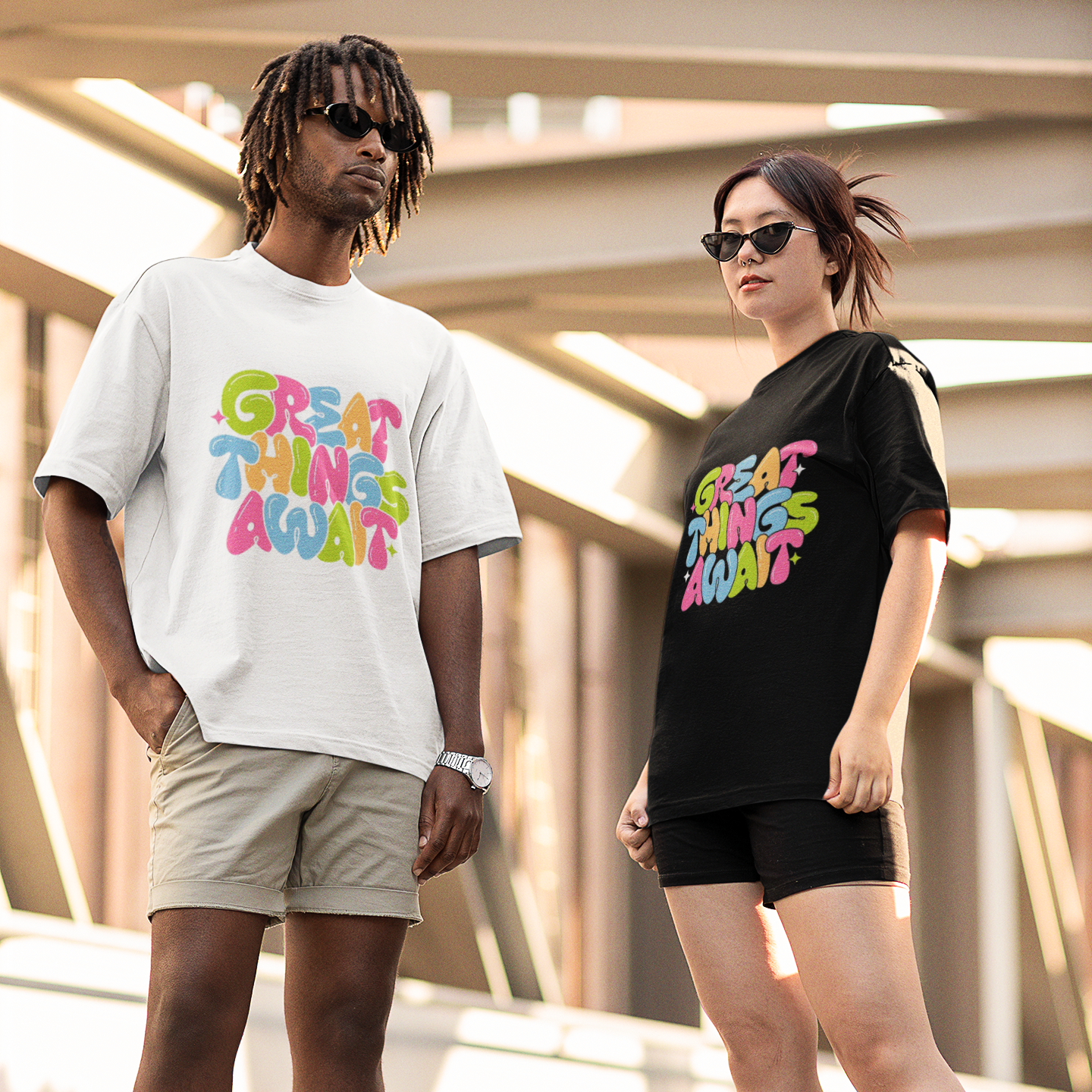 Two people wearing t-shirts with colorful text designs outdoors.