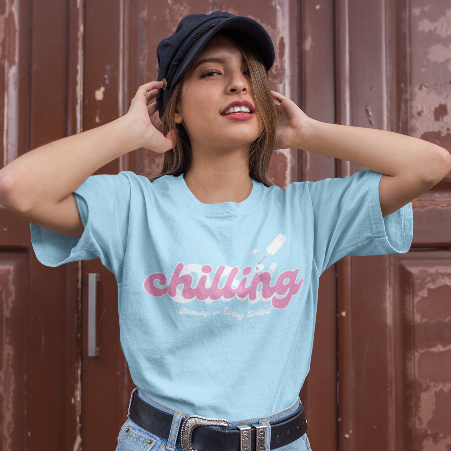 Person wearing a light blue t-shirt with 'chilling' text, denim shorts, and a cap against a brown background.